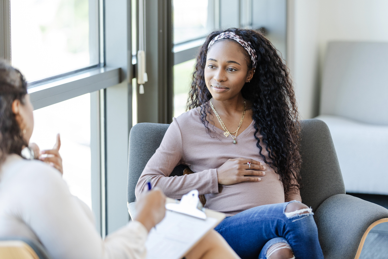 Pregnant person sitting on a couch with a hand on her stomach